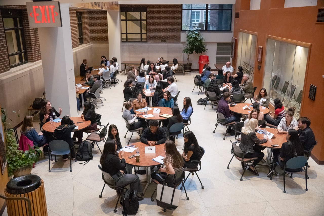 A large room full of round tables with people in professional dress seated and talking