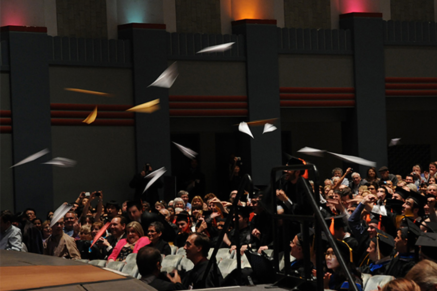 paper airplanes flying toward a stage at a graduation ceremony