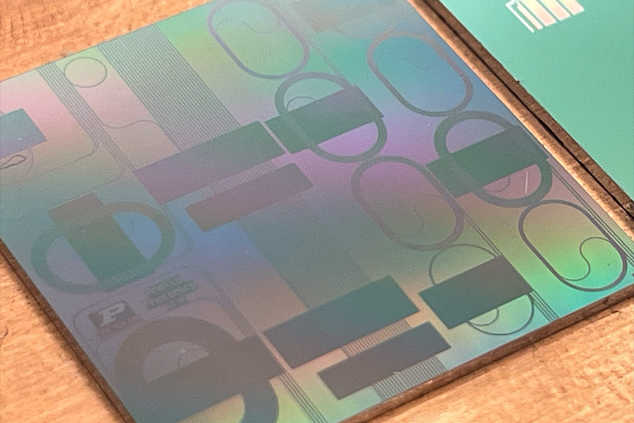 Close-up of a holographic surface featuring abstract geometric patterns with rectangles, circles, and ovals in iridescent hues on a wood table.