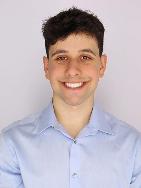 Man with dark hair and dark eyes, smiling, wearing a blue shirt