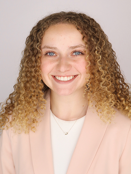 Student with curly blonde hair, blue eyes, smiling, wearing peach blazer