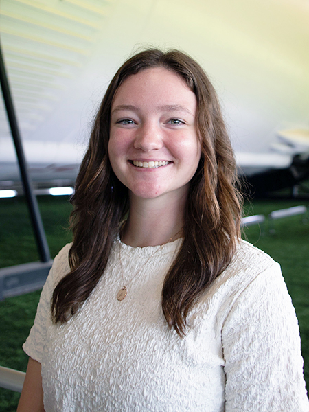 Student with long brown hair, smiling, wearing white blouse