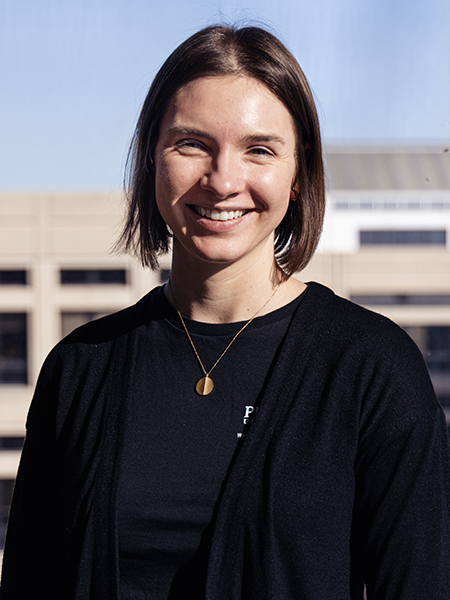 Woman with brown, shoulder-length hair, wearing black shirt, gold necklace, smiling